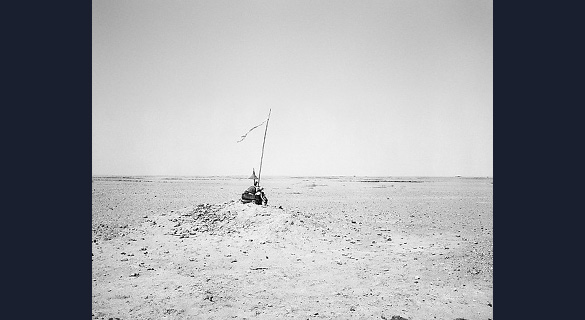 UNIDENTIFIED MEMORIAL IN THE DESERT, SOUTH OF NAMIBE: An assemblage of objects perches on a stony outcrop, surrounded by desert. The long pole protruding from the pile is topped with a ragged banner, announcing the presence of this unusual memorial.