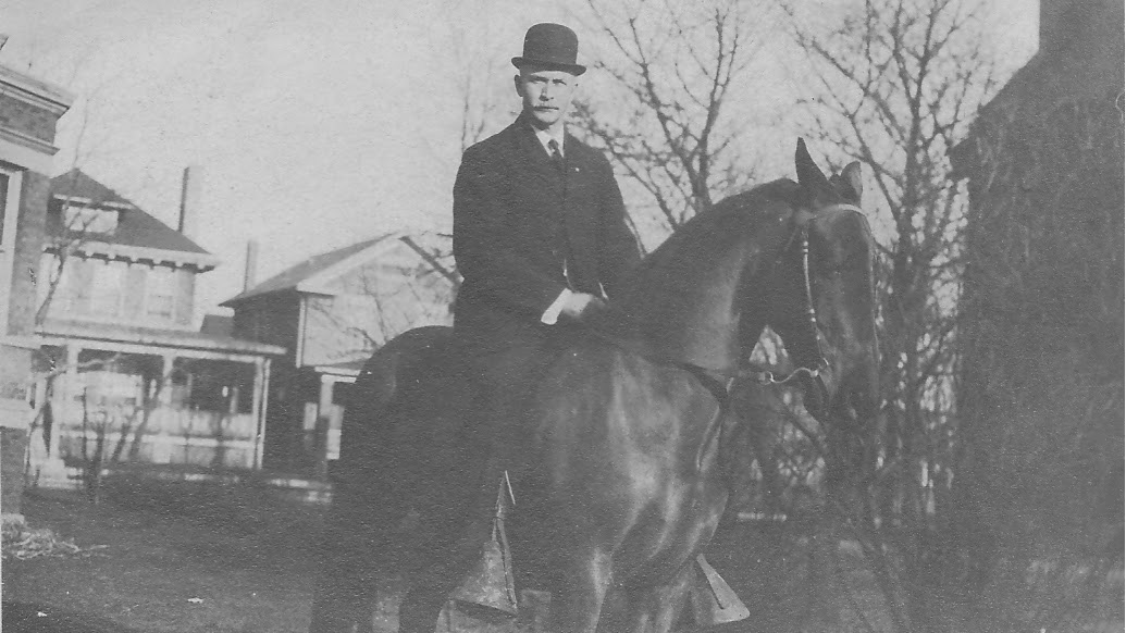 A man in a suit and hat on a horse in black and white