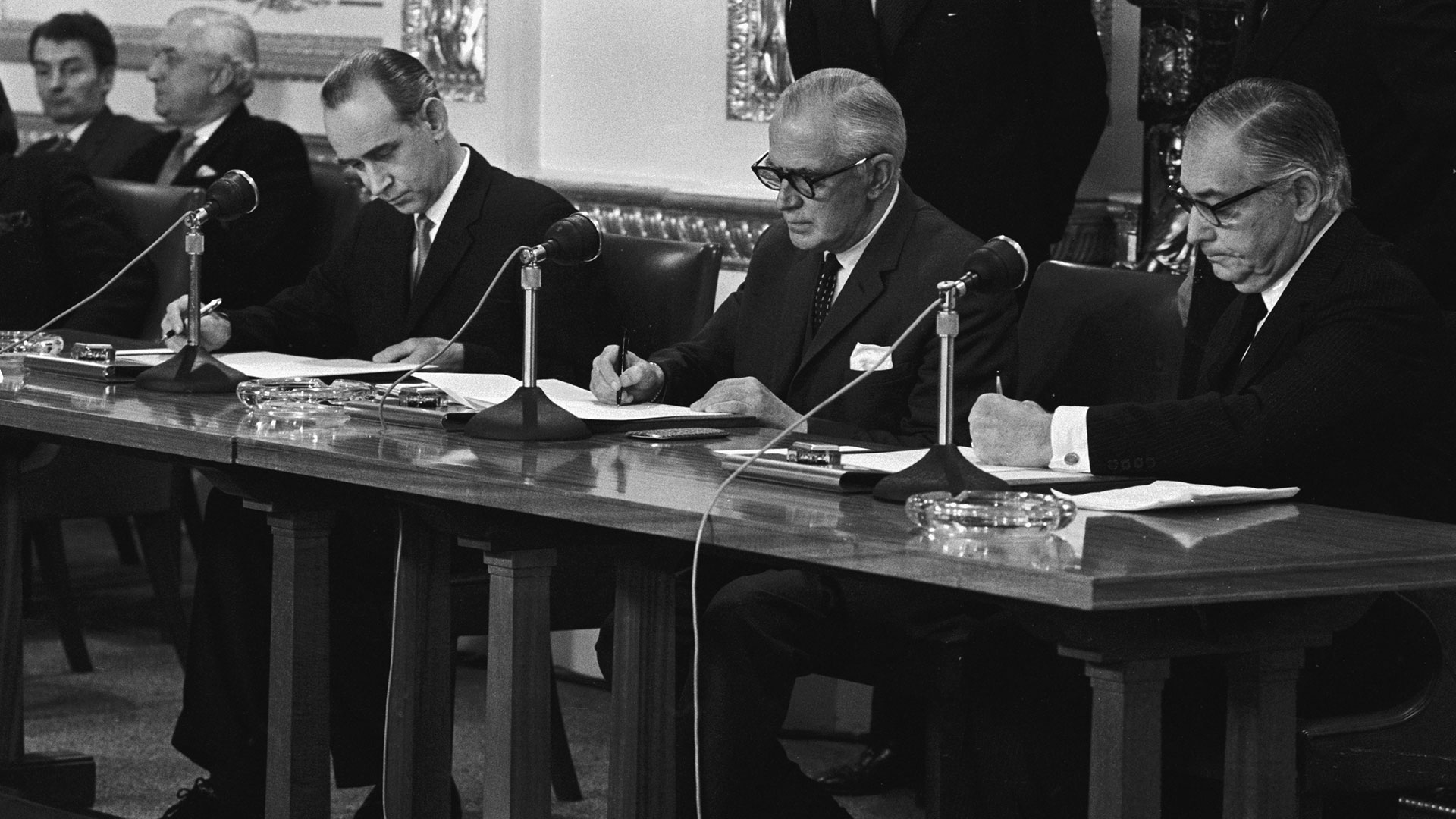 Three men at a press conference in black and white