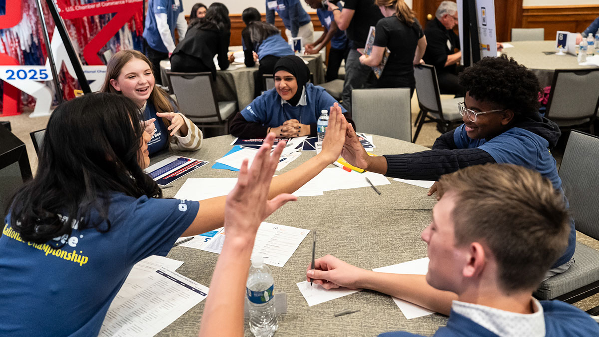 Contestants high-fiving while sitting at a table working together