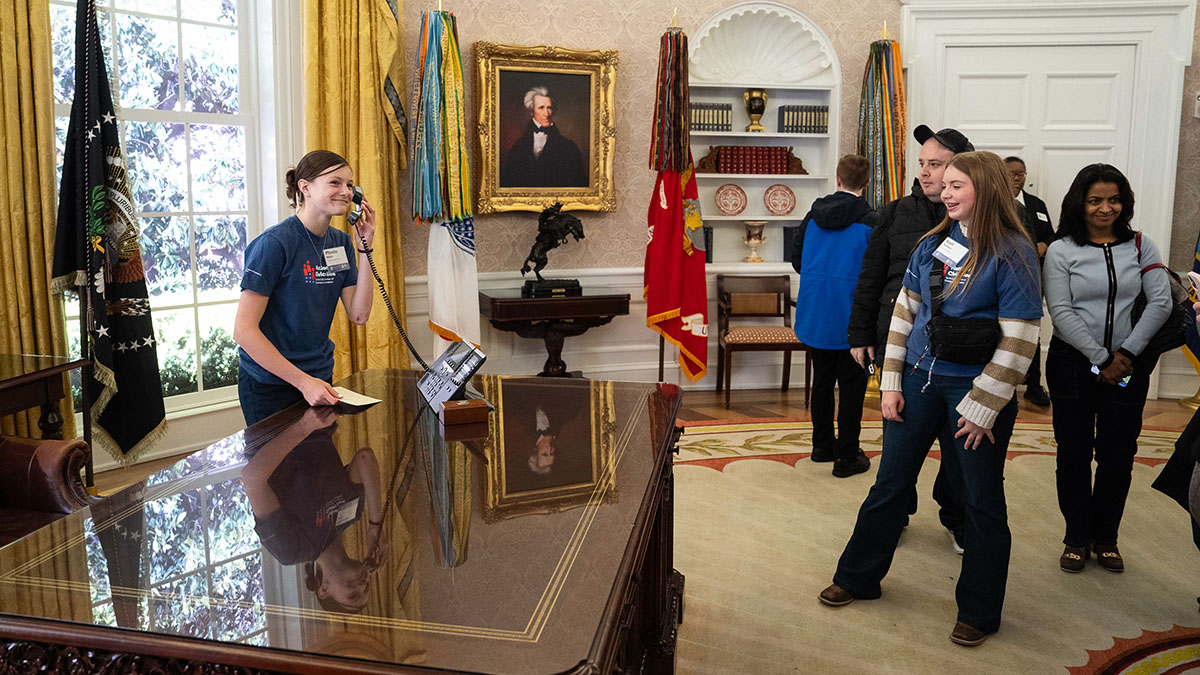 Students touring a replica of the Oval Office with a girl holding the phone on the president's desk