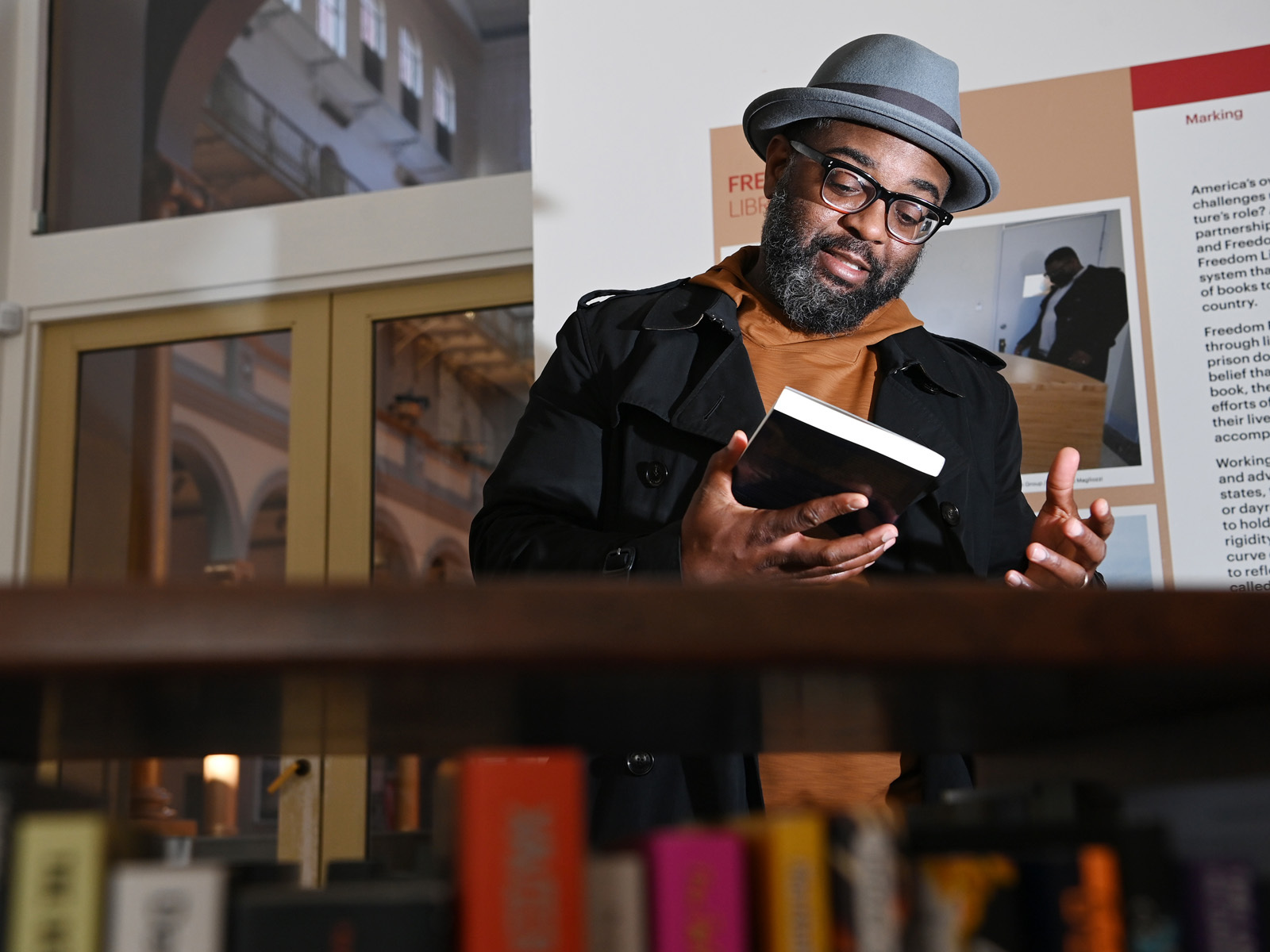 A Black man with glasses and a gray hat holding a book